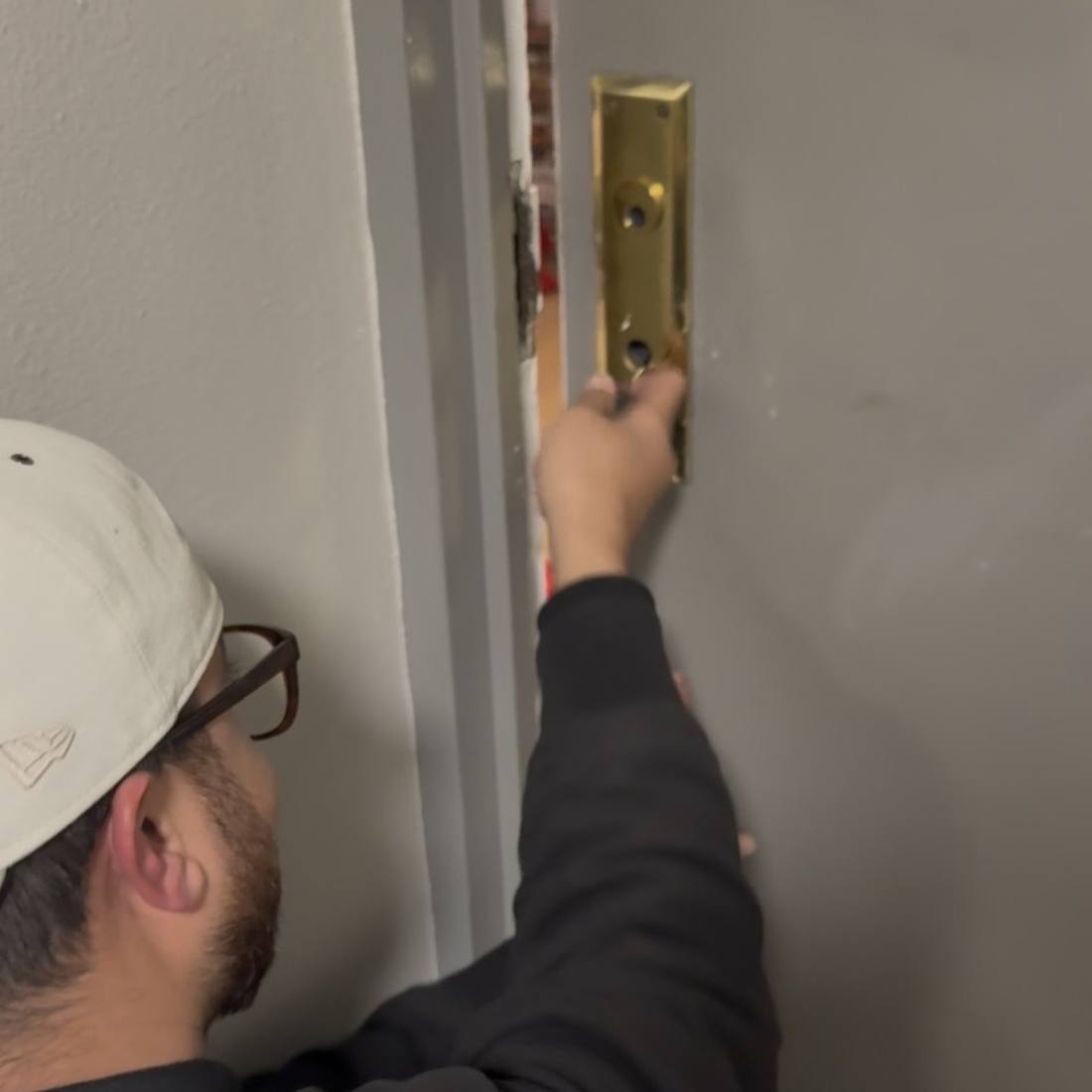 Aura Locksmith technician removing a damaged brass strike plate during an emergency lockout call in Brooklyn